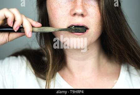Junge Frau ihre Zähne putzen mit einem schwarzen Zahnpasta mit Aktivkohle und schwarzen Zahn Bürste auf weißen Hintergrund für Zähne, die Stockfoto