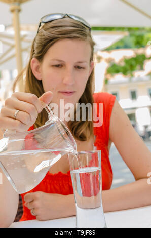 Junge Frau im Restaurant gießt Wasser in ein Glas sitzen. Stockfoto