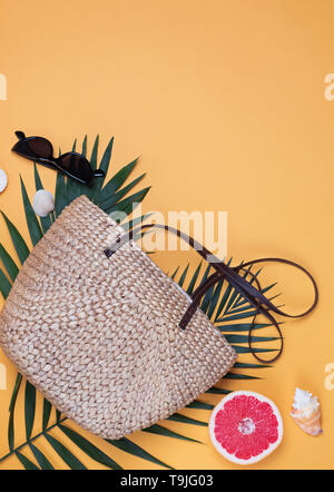 Stilvolle Stroh korb Tasche, Sonnenbrille und Palm Leaf. Kreative Sommer Zusammensetzung auf den gelben Hintergrund. Stockfoto