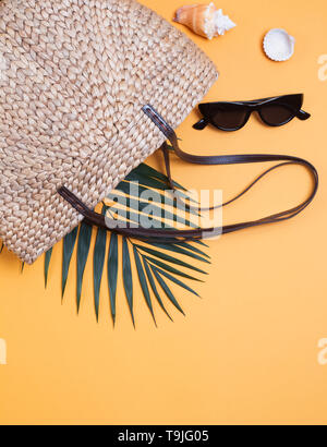 Stilvolle Stroh korb Tasche, Sonnenbrille und Palm Leaf. Kreative Sommer Zusammensetzung auf den gelben Hintergrund. Stockfoto