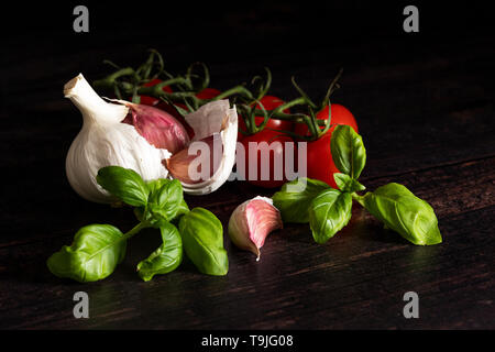 Knoblauch Zwiebel und Knoblauchzehen mit Basilikum und Tomaten auf dunklen Kammer Stockfoto