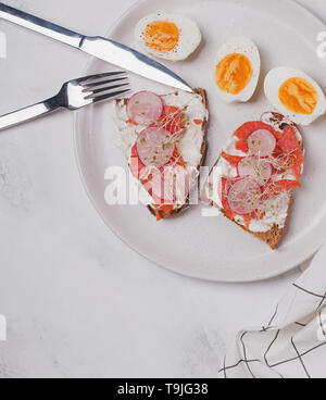 Minimalistische frühstück Foto. Toast mit Frischkäse und Lachs und hart gekochten Eiern auf dem weißen Palte, Ansicht von oben Stockfoto