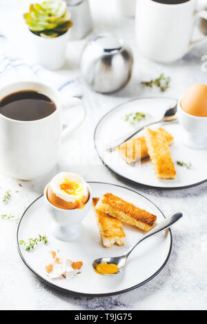 Weich gekochte Eier zum Frühstück mit Toast und Kaffee Tasse im Hintergrund Stockfoto