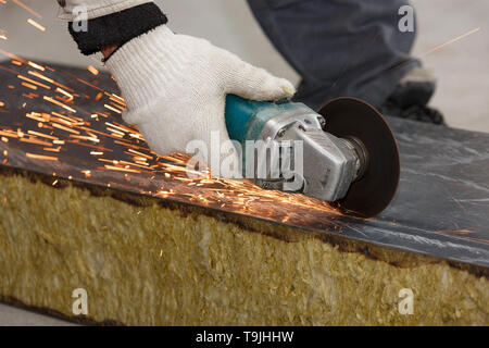 Die Hand eines Arbeitnehmers in einem Handschuh schneidet den Baustoff mit schrägem Schleifmaschine, Erstellen von Funken. Stockfoto