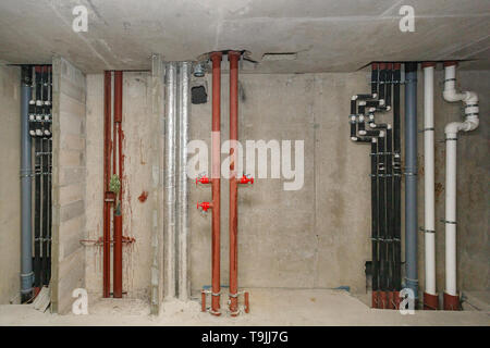 Leitungen von Heizung und Wasserversorgung auf dem Hintergrund einer Betonwand. Stockfoto