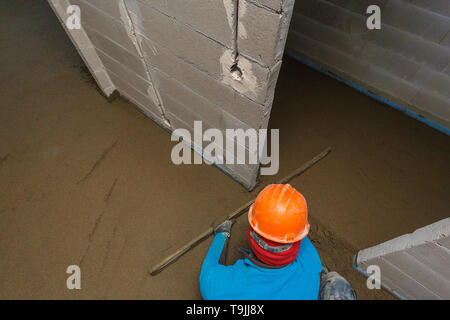Der Arbeiter in einem orange Helm ist die Nivellierung der Estrich Lösung. Stockfoto