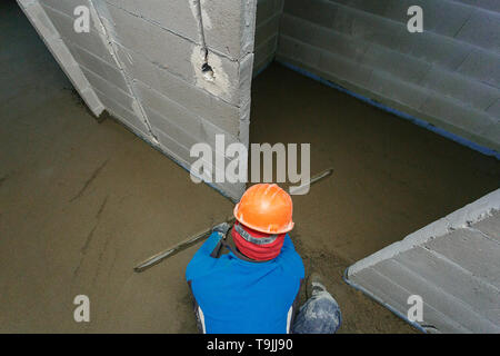 Der Arbeiter in einem orange Helm ist die Nivellierung der Estrich Lösung. Stockfoto