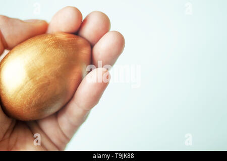 Eine einzige goldene Ei in der Hand auf hellen Hintergrund. Text kopieren. Selektive Weichzeichner. Stockfoto