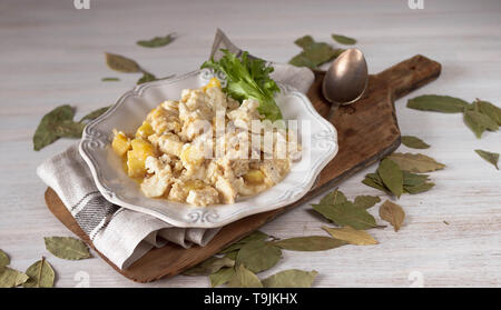 Bacalhau com natas Portugiesische Küche traditionelle Portugal Teller gebackener Kabeljau mit Kartoffeln, Zwiebeln und Sahne in weißem Porzellan Teller Schneidbrett auf Stockfoto