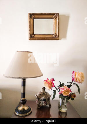 Zwei Rosen in Glas Glas mit Wasser auf den Tisch eines Hauses mit Vintage Dekoration gelegt. Frisch gepflückten Blumen zu Hause mit klassischer Dekoration. Stockfoto