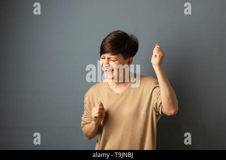 Eine Frau schreit freut sich durch die Wand posieren. Frau Porträt auf grauem Hintergrund. Kopieren Sie Platz. Stockfoto