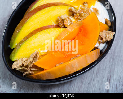 Kürbisscheiben Backen im Ofen, Mango. Haferflocken, Schlagsahne, getrocknete Früchte auf einem Teller mit Kürbis und Mango Stockfoto