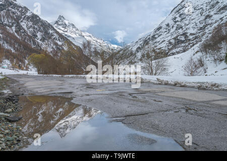 Prominente Peak auf einem noch Wasser Pfütze auf der Straße wider. Scharfe schneebedeckte Gipfel Reflexionen über einen Pool, ein perfektes Spiegelbild eines Berges. Stockfoto