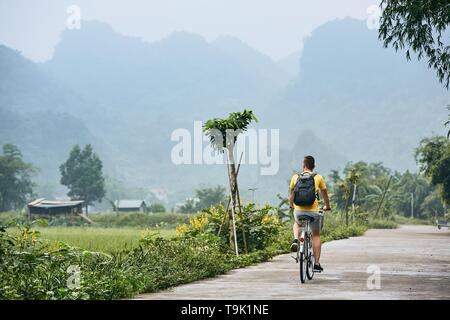 Reise mit dem Fahrrad. Mann mit Rucksack Radfahren auf der Straße gegen karst Bildung in Ninh Binh Provinz, Vietnam. Stockfoto