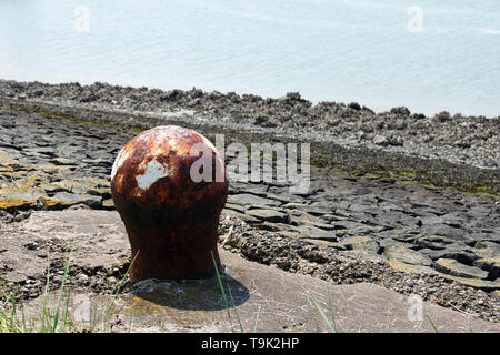 Alte rostige Poller mit ein wenig weiße Farbe und im Hintergrund das Meer Stockfoto