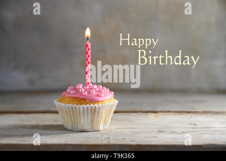 Muffin oder Cupcake mit Rosa brennende Kerze auf einem Holzbrett gegen eine rustikale Hintergrund, Text alles Gute zum Geburtstag, Grußkarte Konzept Stockfoto
