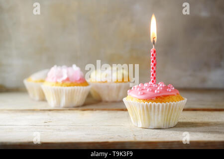 Muffins oder Cupcakes mit einem rosa brennende Kerze auf einem Holzbrett gegen eine rustikale Hintergrund, Geburtstag Konzept mit Kopie Raum, ausgewählte konzentrieren, schmal Stockfoto