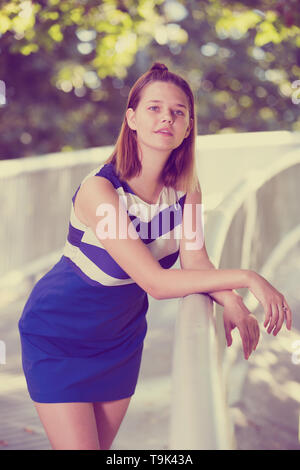 Junge Mädchen in blauem Kleid stehen auf Stadt Brücke umgeben von Bäumen Stockfoto