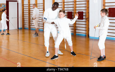 Schwere jungen Fechter aufmerksam zuhören, um professionelle Effiziente freundlich fechten Trainer im Fitnessstudio konzentriert Stockfoto