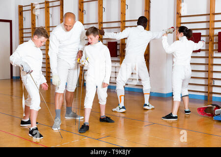 Ernsthafte positive jungen Fechter aufmerksam zuhören zu professionellen, freundlichen fechten Trainer im Fitnessstudio konzentriert Stockfoto