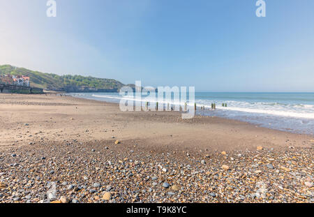 Sandsend in der Nähe von Whitby. Alte hölzerne Wellenbrecher Beiträge führen hinunter zum Strand und einem Vorgewende wird in der Ferne. Bunte Kieselsteine im Vordergrund. Stockfoto