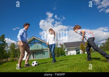 Familie mit Eltern und Sohn Fußball spielen auf dem Hinterhof Rasen in der Nähe von Ihrem Haus Stockfoto