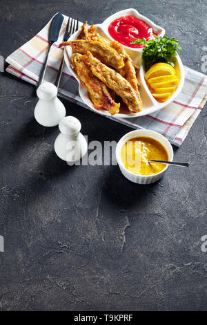 Gebratene kleine capelins mit Tomatensauce, in Scheiben geschnittenen Zitrone auf einer Platte auf einen konkreten Tisch mit Messer und Gabel, vertikale Ansicht von oben Stockfoto