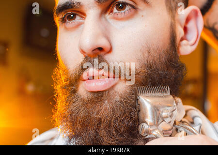 Friseur schneidet einen Bart von Vintage Haarschneidemaschinen, ein junger hübscher Kerl mit Bart und Schnurrbart. Herren Friseursalon. Stockfoto