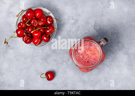 Smoothies sweet cherry in einem marmeladenglas, frische süsse Kirsche auf grauem Beton Hintergrund. Ansicht von oben Stockfoto