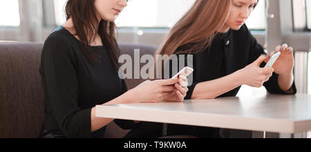 Mitarbeiter können Sie über Ihr Smartphone an einem Tisch in einem Cafe sitzen. Mensch und Technik Stockfoto