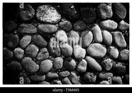 Meer Steine Hintergrund. Abgerundete Steine Textur. Farbige Kopfsteinpflaster. Schwarz-weiß Foto mit Wand aus Steinen in einem weißen Rahmen Stockfoto