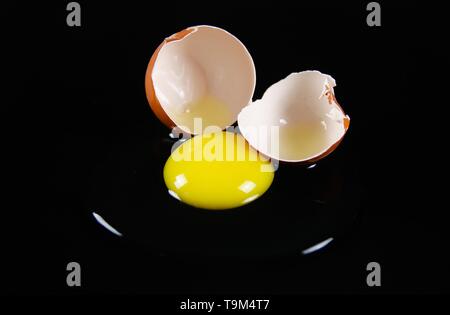 In der Nähe von Brown geknackt Eierschale mit raw-gelb yalk und schleimige Eiweiß auf reflektierenden glänzend schwarzen Hintergrund Stockfoto