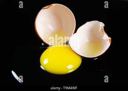In der Nähe von Brown geknackt Eierschale mit raw-gelb yalk und schleimige Eiweiß auf reflektierenden glänzend schwarzen Hintergrund Stockfoto