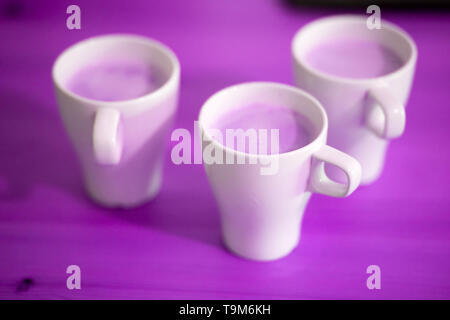 Foto verschwommen, abstrakte lila Farbe, drei Tassen Kaffee auf dem Tisch, Nahaufnahme Stockfoto