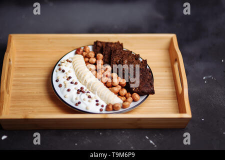 Nahaufnahme von gesundes Frühstück mit Joghurt mit Chocolate Chips, Bananen, Roggenbrot und Haselnuss auf dem Küchentisch Stockfoto