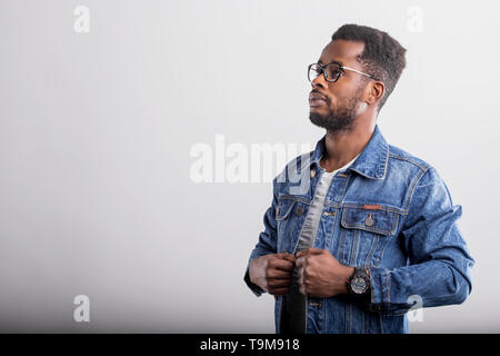 Seitenansicht Portrait von schweren zuversichtlich unrasiert afrikanischen Mann mit vollen Lippen, kurzes lockiges Haar zu tragen Brillen, blau stilvolle Jeansjacke, Uhr, looki Stockfoto