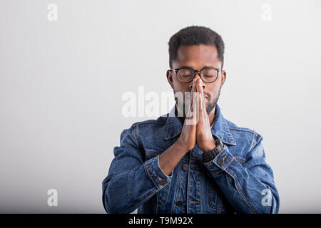 Nahaufnahme des jungen Schwarzen in Brillen beten mit Palmen umklammerten zusammen und geschlossenen Augen, die Gott für viel Glück Erfolg Gesundheit auf Grau backgro Stockfoto