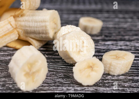 In Scheiben geschnitten und nicht völlig Banane geschält und seine Stücke liegen auf einem dunklen Holz- alten Hintergrund. Das Konzept der Koch eine schnelle gesundes Frühstück Snack Stockfoto
