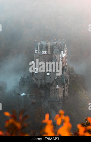 Burg Eltz / Burg Eltz bei Sonnenuntergang an einem nebligen Herbsttag mit Orangenbäumen und Blätter und Nebel rollen durch das Tal (Wierschem, Deutschland) Stockfoto