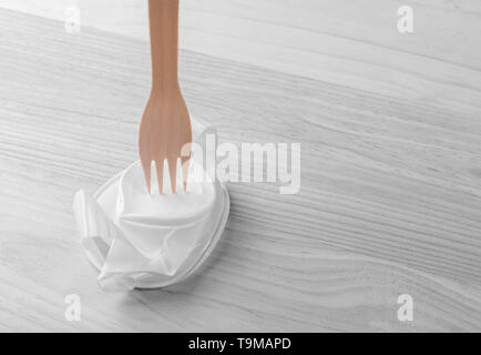 Weiße Schale aus Kunststoff mit einem hölzernen eco Gabel auf dem Holz Tisch zerknittert. Teil des Bild ist schwarz-weiß und farbig. Das Konzept der Kunststoff Stockfoto