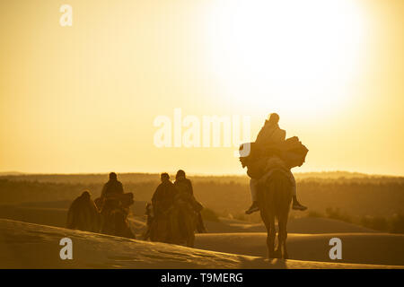 Atemberaubende Aussicht auf einige Touristen reiten Kamele in den Dünen der Wüste Thar in Rajasthan bei einem schönen Sonnenuntergang. Indien. Stockfoto