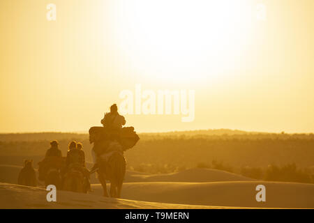 Atemberaubende Aussicht auf einige Touristen reiten Kamele in den Dünen der Wüste Thar in Rajasthan bei einem schönen Sonnenuntergang. Indien. Stockfoto