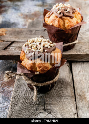 Zwei Muffins mit Milch Schokolade und Nüsse auf einem rustikalen Holzmöbeln Hintergrund. Close-up Stockfoto