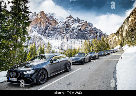 Die große Gruppe teurer Sportwagen macht auf der kurvenreichen Straße in den Alpen gegen schneebedeckte Berge Halt Dolomit, Mercedes Benz, Porsche Stockfoto