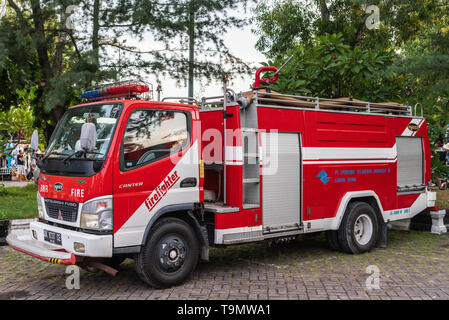 Bali, Indonesien - Februar 25, 2019: Nahaufnahme von roten und weißen Fire Truck Unter grünem Laub in Denpasar geparkt. Stockfoto