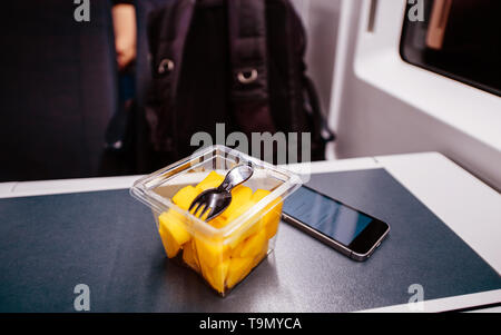 Wassermelonen Salat mit der Gabel - Reisen in schnellen Bahn in Großbritannien kleine Smartphone auf dem Tisch Stockfoto