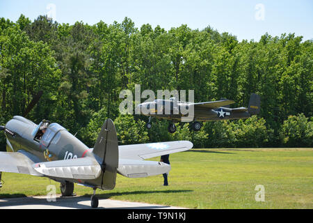 Ein vintage Mitchell B-25 Bomber zieht vorbei an einer Curtiss P-40 Warhawk während des 2019 Virginia Beach militärische Luftfahrt Museum WWII zeigen. Stockfoto