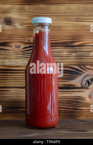 Glas Flasche Tomatenmark mit rohen frische organische Tomaten auf Holzuntergrund Stockfoto