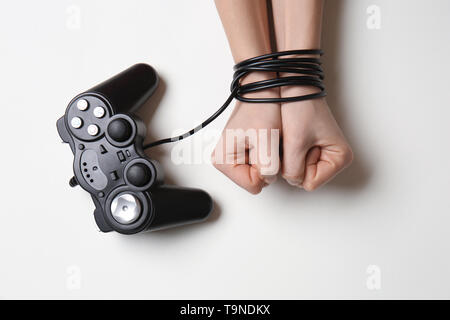 Weibliche Hände gebunden mit Kabel des Joystick auf weißem Hintergrund. Konzept der Neigung Stockfoto