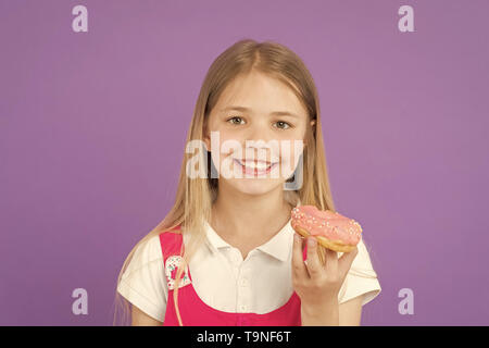 Kind Lächeln mit Donut auf Violett Hintergrund. Kleines Mädchen mit glasierten ring Donut. Glückliches Kind mit Junk Food auf lila Hintergrund. Essen und Nachtisch. C Stockfoto